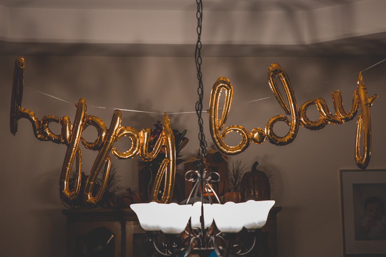 Home Festive gold balloons spelling 'happy bday' hang indoors, ideal for party themes.